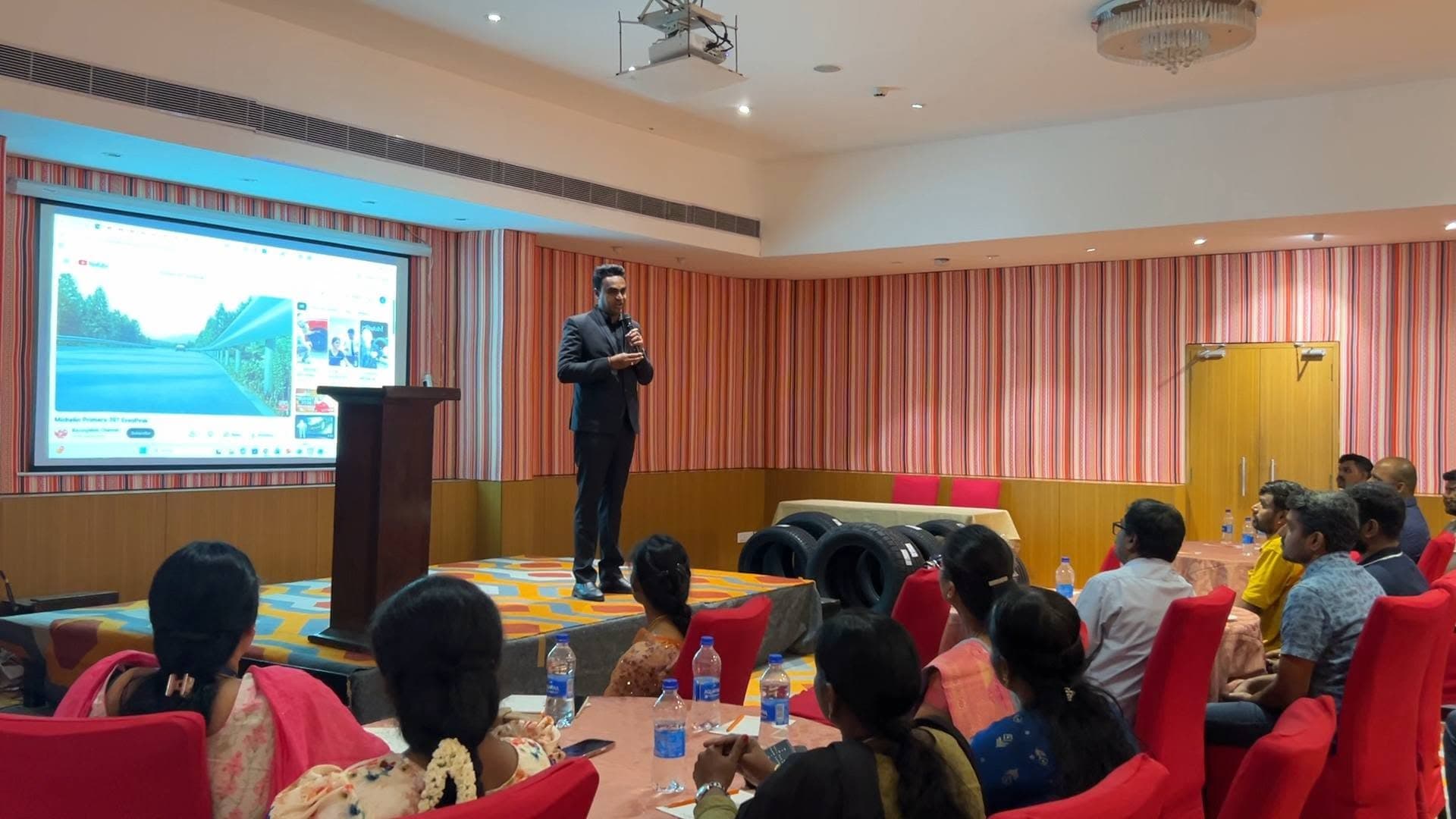 Manesh on stage addressing a seated corporate audience
