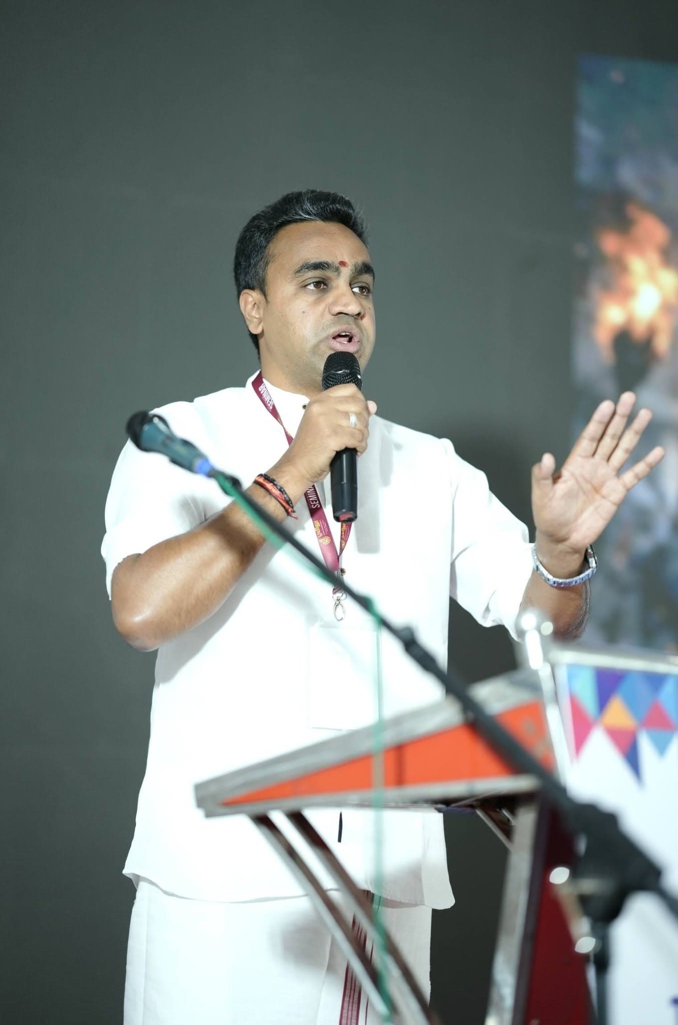Manesh Chandran speaking at a lectern with one hand raised